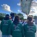 3 personnes de dos avec des vestes vertes floquées du logo officiel des CRTE "Le cheval, naturellement". Une des personnes porte une bannière représentant une tête de cheval avec des brins de blés et et fleurs sur le pourtour.